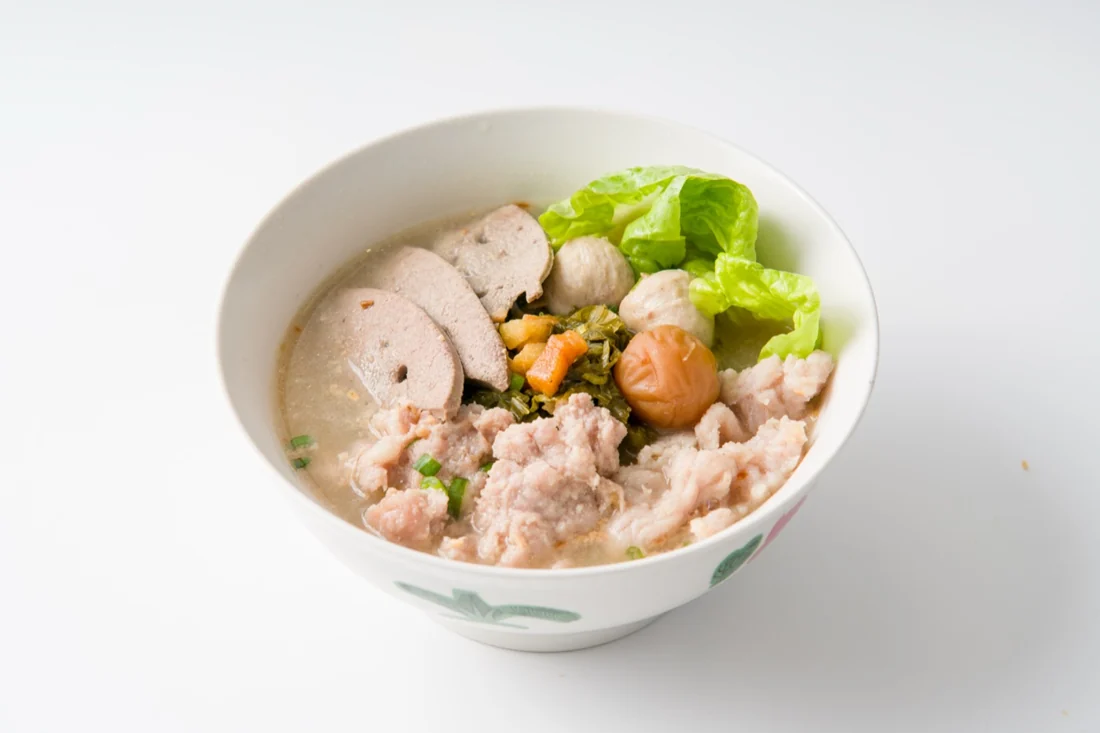 A bowl of pork noodles topped with pork slices, minced pork, meatballs and greens